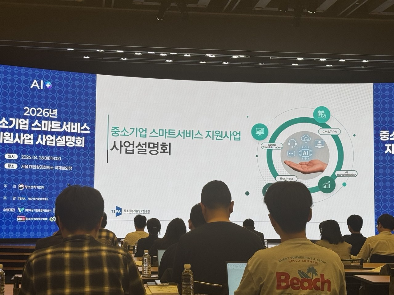 설명회 강연장 풍경 — 메인 스크린에 사업설명회 타이틀과 참석자들