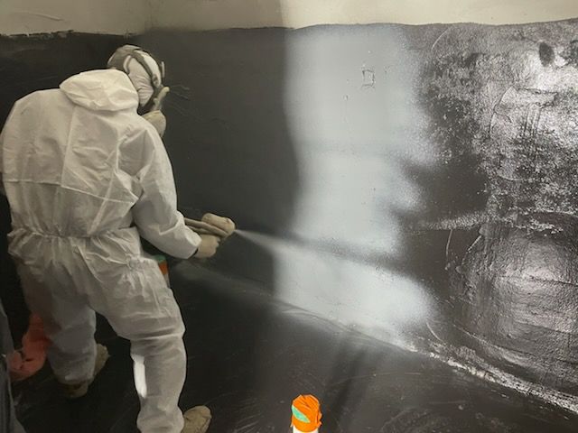 폴리우레아 벽면 도포 — 벽면 절반이 검은색으로 코팅되어 도포 전후 대비가 보인다