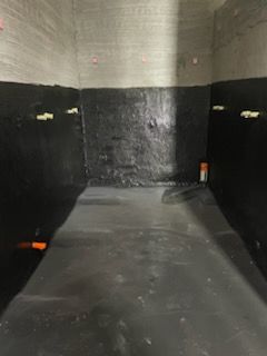 우레탄 중도 완료 — 개별 샤워 부스 내부. 벽면과 바닥이 검은색 우레탄으로 코팅. 수전 밸브(주황색 캡)가 보인다