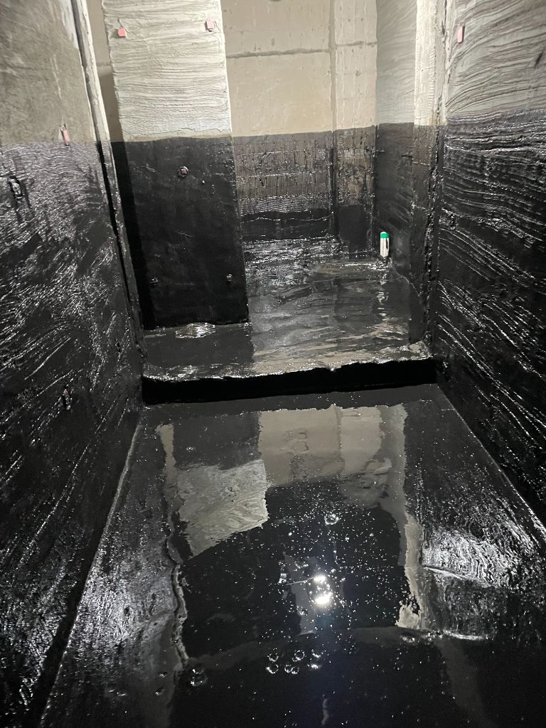 우레탄 중도 도포 직후 — 바닥이 거울처럼 반사되는 젖은 상태. 칸막이벽 하단까지 검은색 코팅