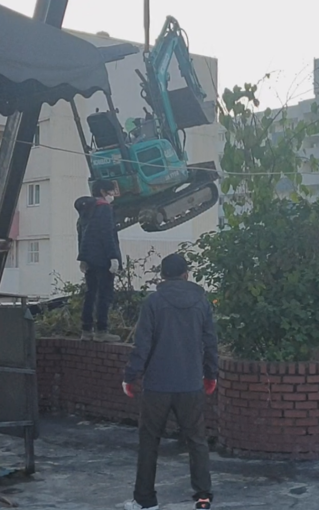 옥상에서 본 크레인 장비 투입 장면 — 작업자가 장비를 유도하는 모습
