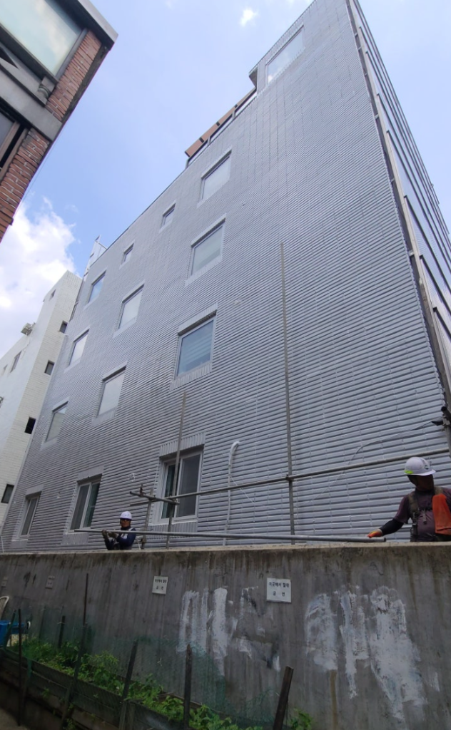 시공 후 건물 측면 — 회색 매직탄 수평줄무늬 마감 완료, 아시바 철거 중