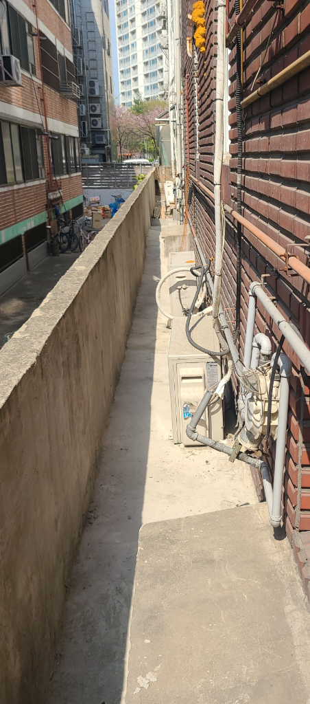 건물 측면 통로 전경 — 벽돌 외벽 줄눈 노후화, 배관 관통부 코킹 열화 상태