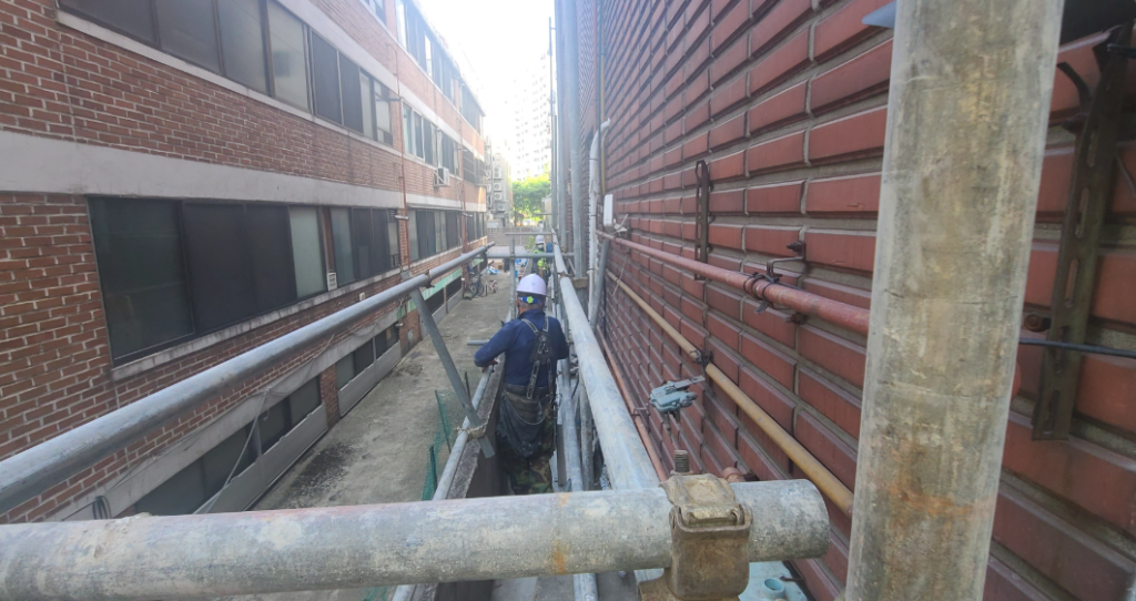 아시바 상부에서 바라본 외벽 — 작업자가 비계 위에서 작업 중