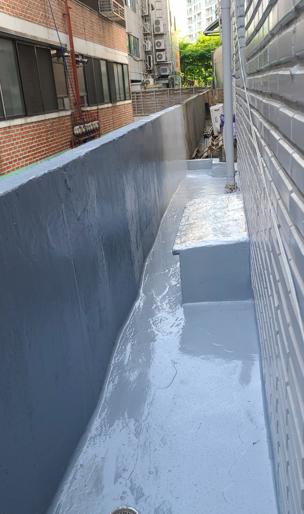 1층 바닥 우레탄 중도 완료 — 좁은 통로 바닥과 벽면 하단부 전체에 회색-청회색 방수재가 균일하게 도포된 상태, 표면에 광택이 남아 있음