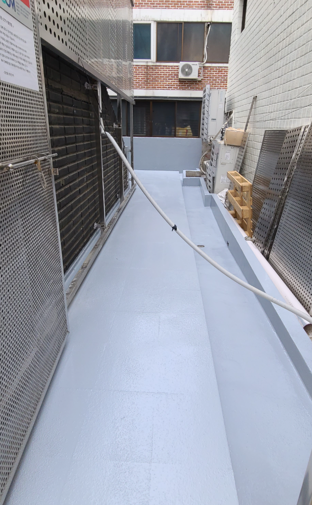 1층 바닥 상도 마감 완료 — 좁은 통로 전체에 밝은 회색 우레탄 방수가 깔끔하게 마감된 모습, 벽면 하단까지 방수 처리 완료